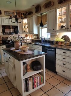 a kitchen with white cabinets and black counter tops, an island in the middle has books on it