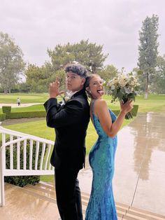 a man and woman standing next to each other in front of a white fence holding flowers