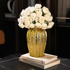 a gold vase filled with white flowers on top of two books