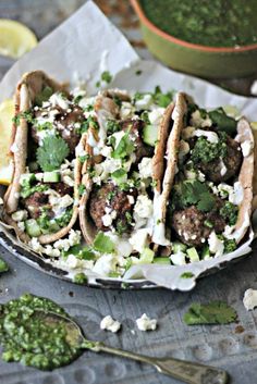 three tacos filled with meat and vegetables on top of a table next to lemon wedges