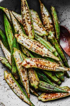 grilled green beans in a white bowl with a spoon and pepper flakes on the side