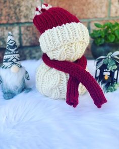 a knitted snowman sitting on top of a white blanket next to two small gnomes