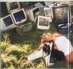 a woman laying on the ground surrounded by old televisions