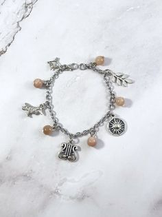 a bracelet with charms on it sitting on top of a white marble countertop next to a silver chain