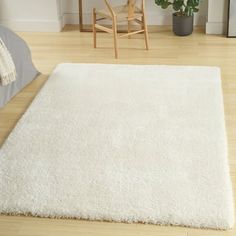 a large white rug on the floor in a living room with a chair and potted plant