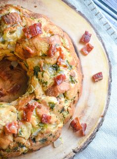 there is a bundt cake with bacon and cheese on the top it sits on a wooden plate