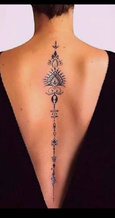 the back of a woman's neck with an intricate tattoo design on her lower back