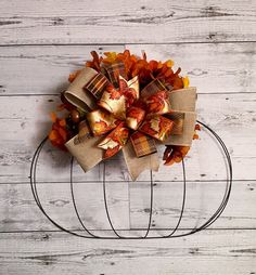 a wreath made out of burlocks and fall leaves on a wire stand against a white wooden wall