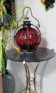 a glass table topped with a red ball on top of a metal stand next to a potted plant