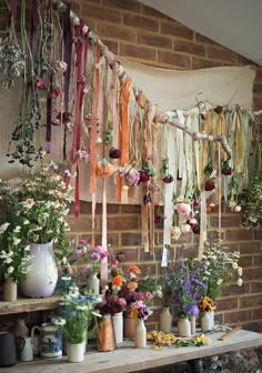 a bunch of flowers are hanging on the wall in front of a brick wall and some vases