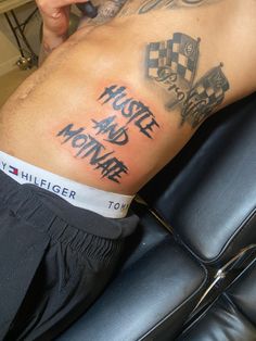 a man with tattoos on his stomach sitting in a chair holding a cell phone to his ear