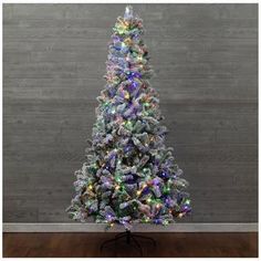 a white christmas tree with multicolored lights in front of a gray wall and wooden floor