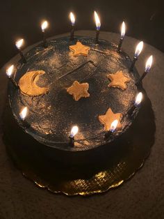 a black cake with gold stars and moon decorations on it, surrounded by lit candles