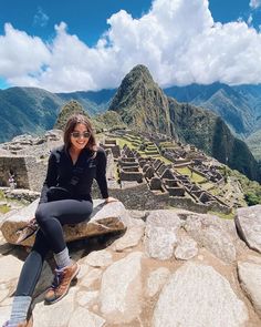 a woman sitting on top of a stone wall next to a mountain with a valley in the background