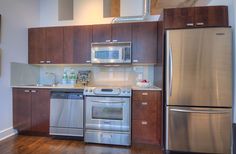 an empty kitchen with stainless steel appliances and wood flooring is pictured in this image