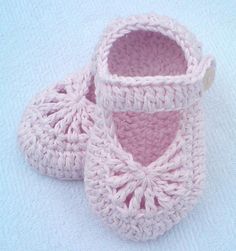 a pair of pink crocheted baby shoes sitting on top of a white blanket