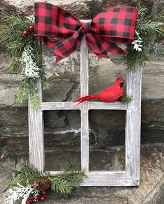 a red cardinal sitting on top of a wooden window frame with pine cones and berries