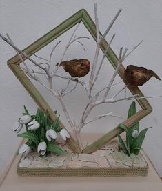 two birds sitting on top of a tree branch in front of a frame with flowers