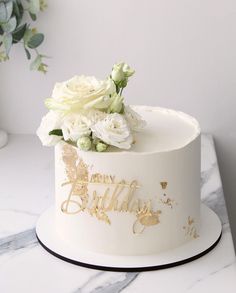 a white and gold birthday cake with flowers on top