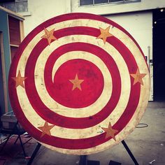 a large red and white target with gold stars on the center in front of a building