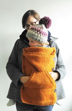 a woman holding a child wearing an orange sweater