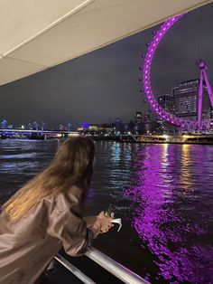 a woman is looking at the ferris wheel in the distance while standing on a boat