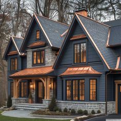 a blue house with copper roofing and two story windows in the front, surrounded by trees