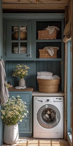 a washer and dryer in a small room with blue cabinets, white towels and flowers