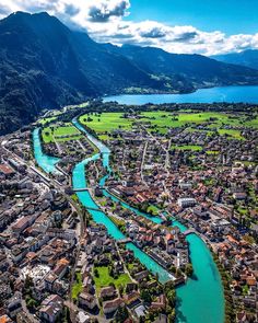 an aerial view of a river running through a small town with mountains in the background