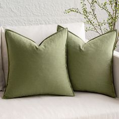 two green pillows sitting on top of a white couch next to a vase with flowers