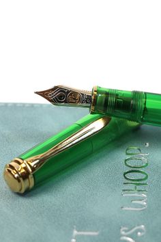 a green fountain pen sitting on top of a blue book with gold trimmings