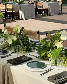 the table is set with plates, silverware and green flowers in vases on it