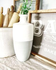 a white vase sitting on top of a table next to a framed sign and potted plant