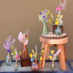 several vases filled with flowers sitting on top of a wooden table next to a stool