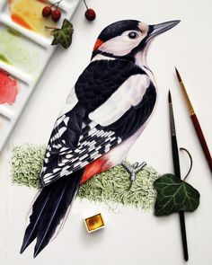 a bird sitting on top of a piece of paper next to some paintbrushes