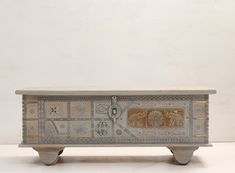 an ornately decorated chest on wheels stands against a white wall, with gold and silver accents