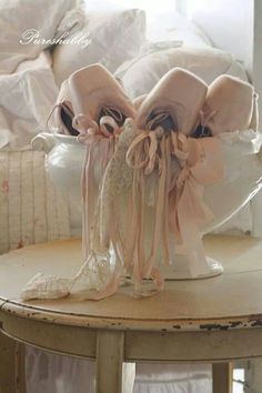 a white vase filled with lots of pink ribbons on top of a table next to a pile of pillows