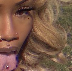 a close up of a person with piercings on her nose and tongue sticking out