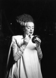 a woman in a white dress is holding a hair dryer and looking down at her face