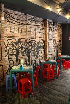 an empty restaurant with colorful tables and chairs in front of a brick wall that has graffiti on it