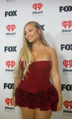 a woman in a red dress standing on a red carpet with her hands behind her back