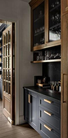 a kitchen with wooden cabinets and black counter tops, along with wine glasses on the shelves