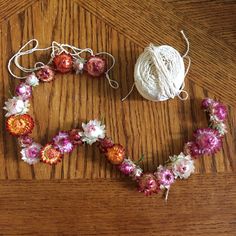 yarn and flowers arranged in the shape of a heart on a wooden table next to a ball of string