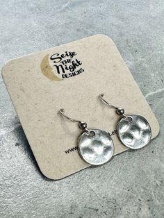 - Get ready to rock the quirky silver disc earrings! These small hammered discs have a 15mm diameter and a sweet 27mm drop. Made with stainless steel ear wires, they come on a branded card with clear ear backs. Unconventionally stylish and versatile, these hammered silver disc earrings will add a touch of cool to any outfit. With a 15mm diameter and 27mm drop, they're perfect for any occasion. Crafted with durable stainless steel ear wires, these earrings come on a branded card with clear ear ba Indiana Love, Baby Jewelry, Bag Icon, Garden Print, Disc Earrings, Print Book, Ear Wires, Hammered Silver, Corporate Gifts