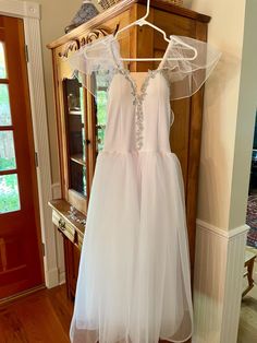 a white dress hanging on a hanger in front of a wooden cabinet and door