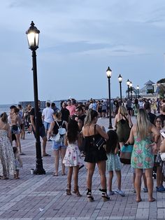 a group of people standing on top of a sidewalk next to a light pole and street lamp