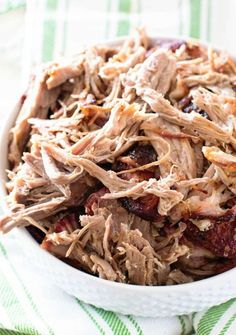 a white bowl filled with shredded meat on top of a green and white towel