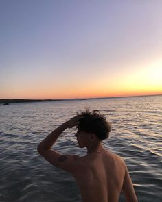 a shirtless man standing in the water at sunset