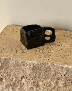 a small black vase sitting on top of a stone slab next to a white wall