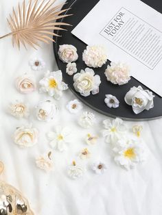 white flowers on a black plate next to an open book and some goldware with a palm leaf